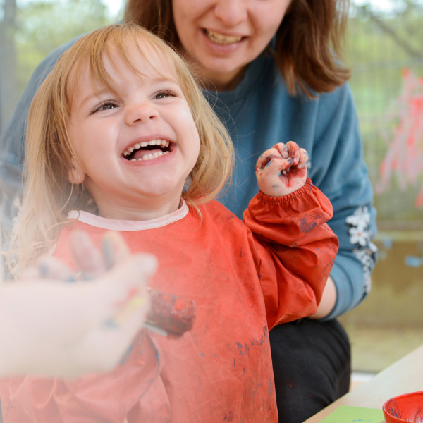 Lachendes Kind in Malschürze genießt das Malen mit Farben im inklusiven Kinderzentrum.