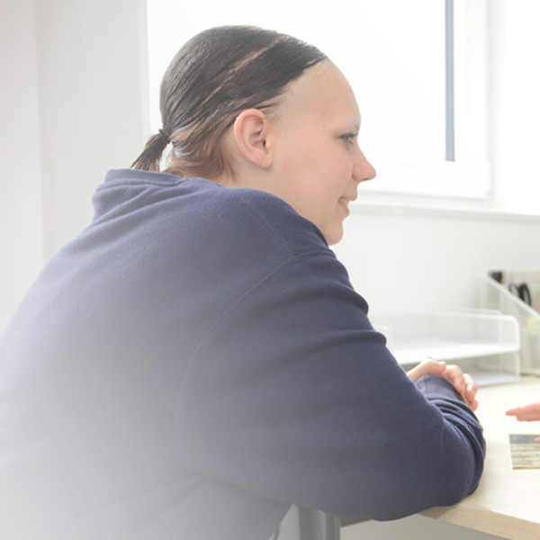 Eine Frau hilft einer anderen Frau. Sie sprechen an einem Tisch. Es sieht aus wie eine Beratungsstelle.