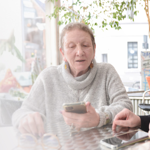 Zwei Frauen sitzen an einem Tisch in einem Café. Eine Frau hält ein Handy in der Hand. Sie sprechen miteinander.