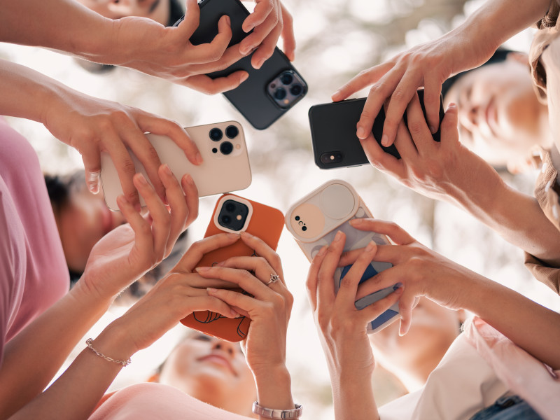 Blick von unten in einen Kreis von Handys, die Jugendliche in den Händen halten und im Blick haben.