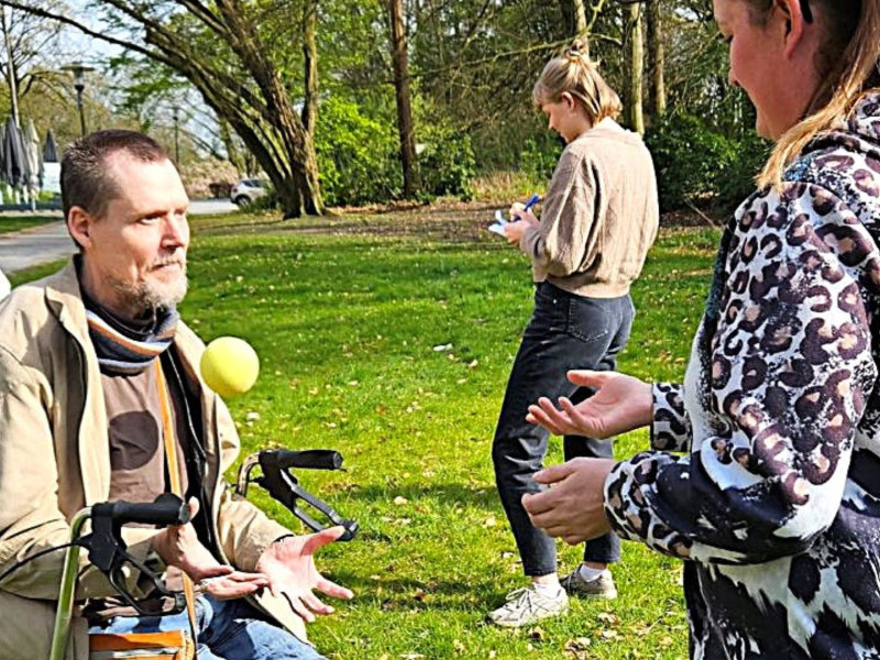 Mann mit Rollator und Mehrfachbehinderung übt Ballkoordination im Freien mit Unterstützung, Aktivitätsförderung für Menschen mit Behinderung