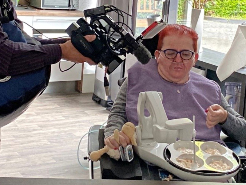 Ein Kamerateam dokumentiert den Einsatz eines assistiven Essroboters für Menschen mit körperlicher Behinderung in einer barrierefreien Pflege- und Wohnumgebung.