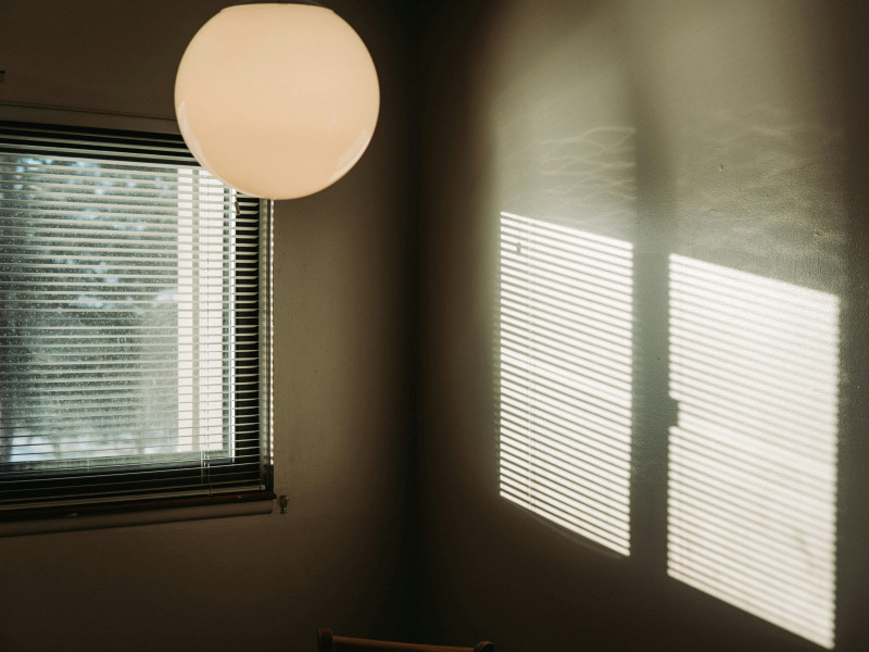 Sonnenlicht fällt durch Jalousien und wirft Streifenmuster auf eine Innenwand.