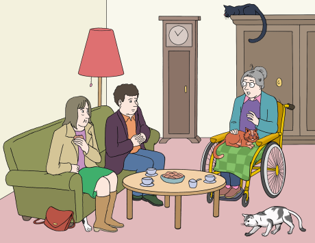 Drei Menschen unterhalten sich im Wohnzimmer. Zwei Katzen sind dabei.