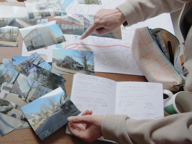 Ein Finger zeigt auf eine Karte, um die herum mehrere Fotos und ein Notizbuch zu sehen sind