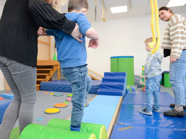 Kinder balancieren auf einem Spielgerät, unterstützt von Erwachsenen.