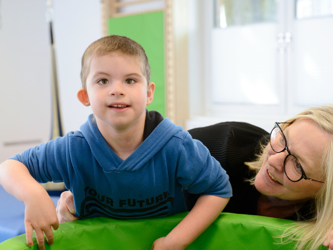 Lächelndes Kind in einem blauen Pullover spielt mit einer Erwachsenen im inklusiven Kinderzentrum