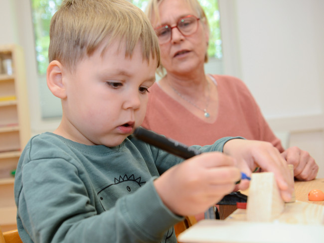 Kind konzentriert sich auf eine Bastelarbeit, während eine Erwachsene zuschaut.