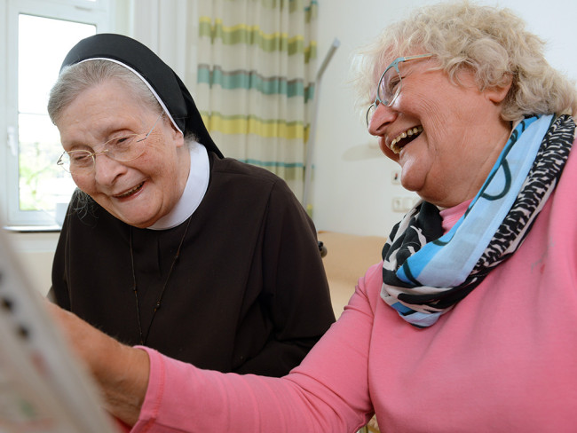 Zwei ältere Frauen lachen zusammen und schauen sich etwas an.
