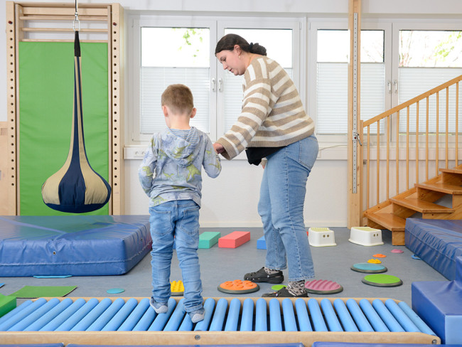 Eine Frau hilft einem Kind beim Balancieren in einem Spielzimmer.