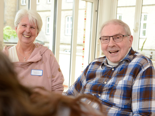 Zwei ältere Menschen lächeln glücklich in einem hellen Raum.