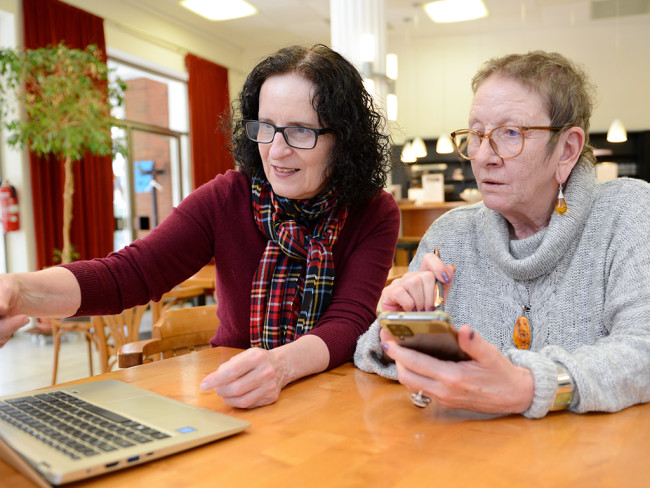 Zwei Frauen arbeiten zusammen an einem Laptop und Smartphone in einem Café.