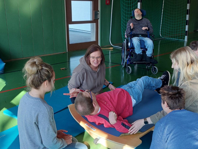 Menschen mit Mehrfachbehinderung beim gemeinsamen Bewegungstraining in einer Sporthalle, betreut von Fachpersonal