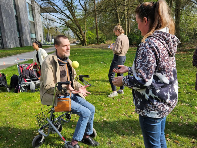 Mann mit Rollator und Mehrfachbehinderung übt Ballkoordination im Freien mit Unterstützung, Aktivitätsförderung für Menschen mit Behinderung