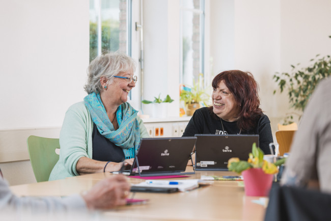 zwei ältere Damen unterhalten sich vor zwei Laptops