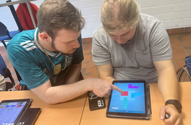 Zwei Menschen beugen sich über ein Tablet, einer zeigt auf dem Bildschirm auf etwas.