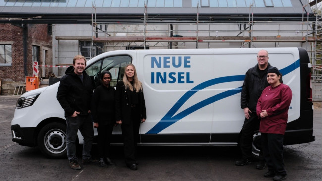 Fünf Personen stehen nebeneinander vor weißem Lieferwagen mit „Neue Insel“-Logo, Baustellenkulisse im Hintergrund