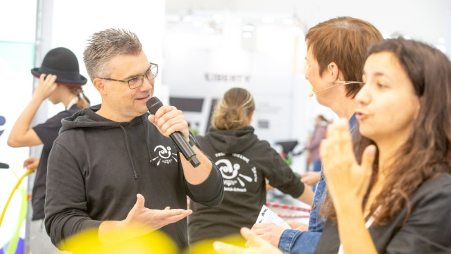Mann mit Mikrofon spricht auf der REHACARE, daneben Dolmetscherin in Gebärdensprache – barrierefreie Kommunikation im Fokus.