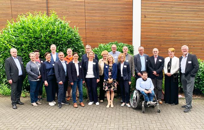 Gruppenfoto des STUFE-Beirats mit Teilnehmenden aus Wissenschaft, Praxis und Trägerschaft vor Holzfassade – Projektvorstellung auf der REHACARE 2025 in Düsseldorf