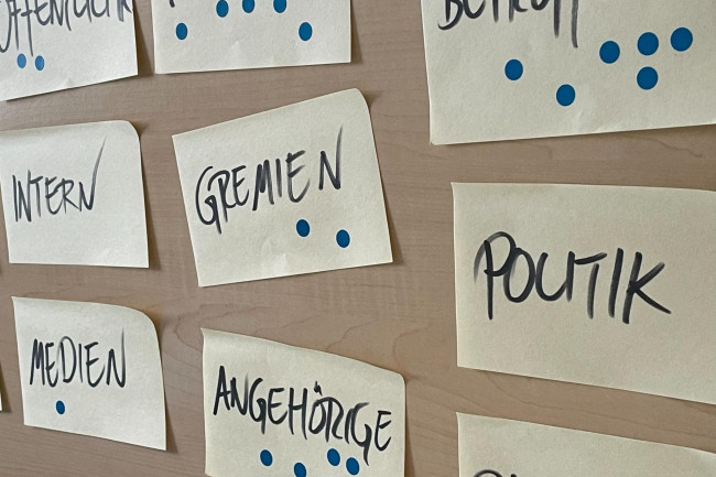 auf einem Pinnwandausschnitt hängen Zettel mit den Schlagworten: Intern, Gremien, Politik, Angehörige, Medien, u.a.
