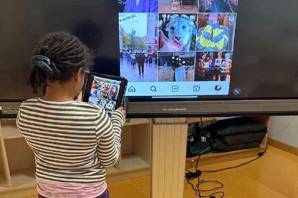 Mädchen steht mit Tablet vor großem Bildschirm