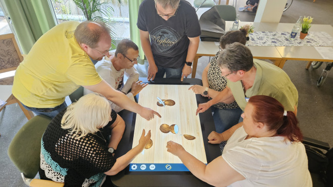 Eine Gruppe Senior:innen beugt sich gemeinsam über einen Aktivitätstisch.