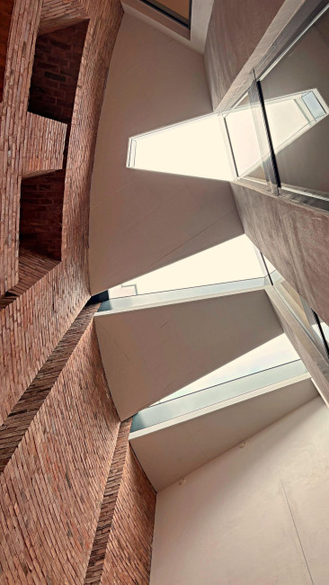 Blick nach oben in die ehemalige Kirche St. Peter Morus in Leverkusen mit hohen Backsteinwänden und schmalen Oberlichtern, die Tageslicht in den Raum lenken.