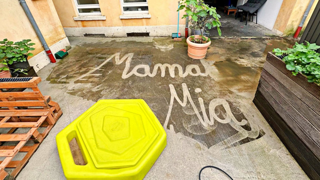 Mit Wasser auf Beton geschriebener Schriftzug ‚Mama Mia‘ in einem Innenhof