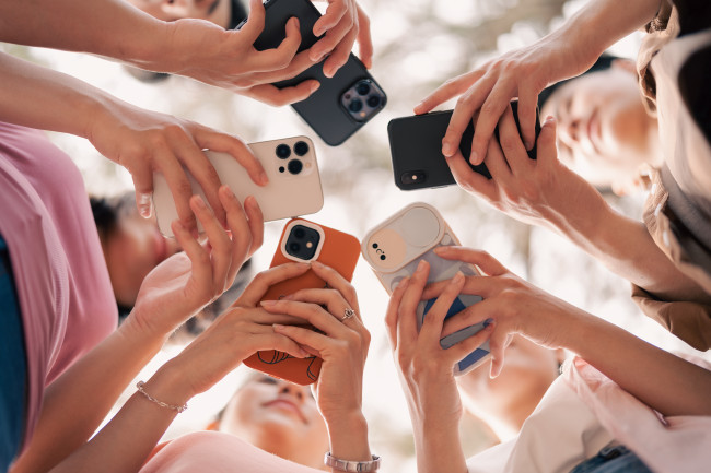Blick von unten in einen Kreis von Handys, die Jugendliche in den Händen halten und im Blick haben.