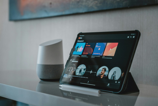 Tablet mit Musik-Streaming-App neben einem Smart Speaker auf einem Tisch.